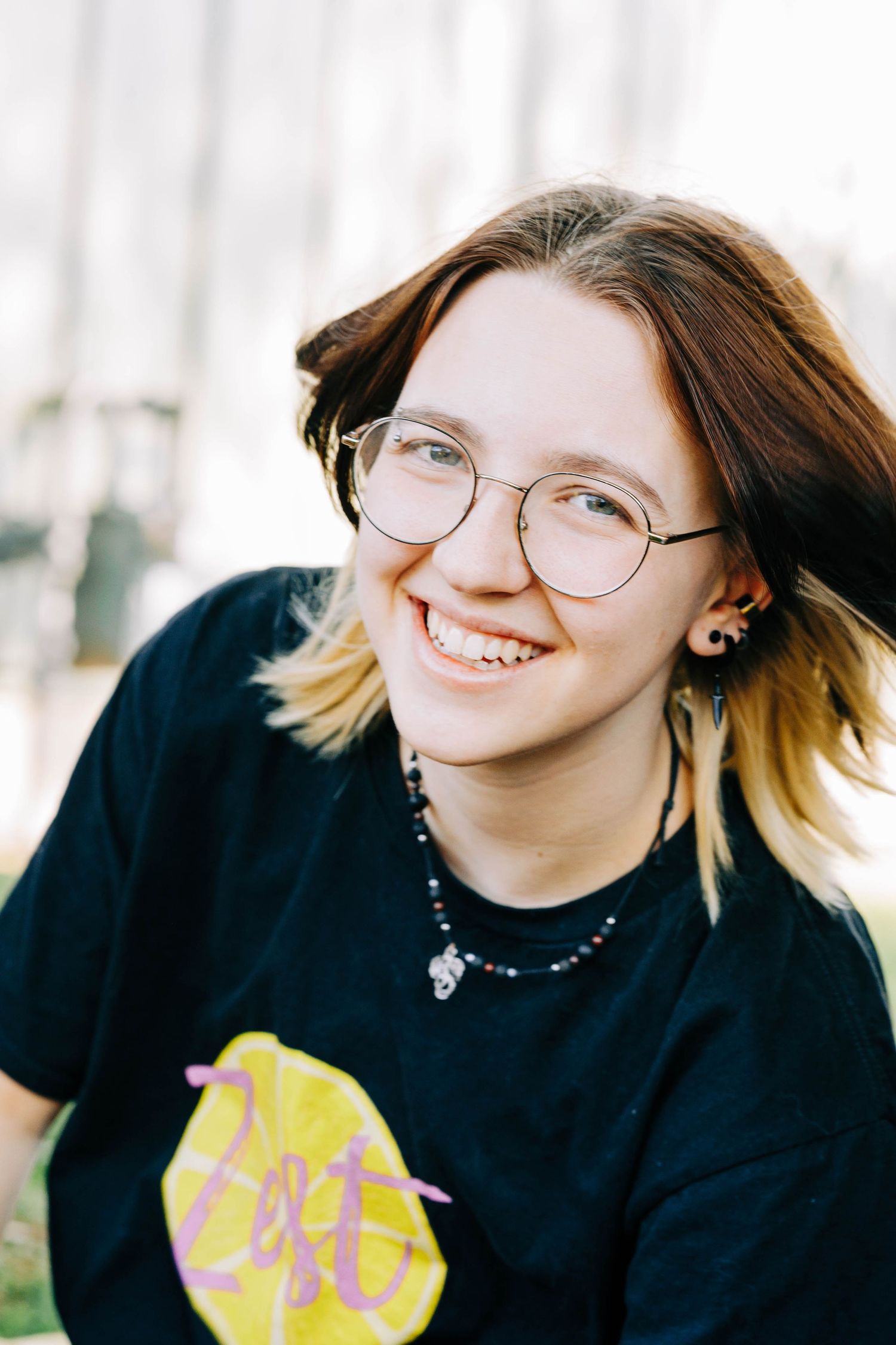 Smiling teenage girl with round glasses and dark hair wearing black Zest graphic tee.