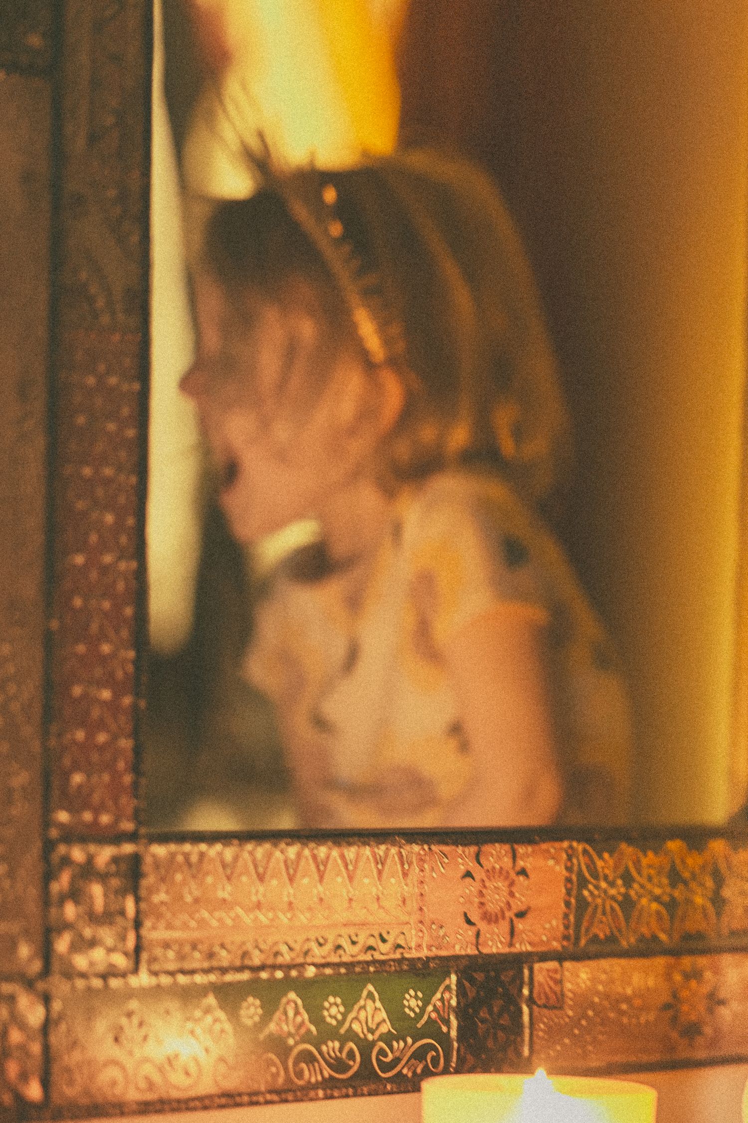Blurred reflection of a young girl wearing a headband seen through an ornate golden mirror frame with candle.