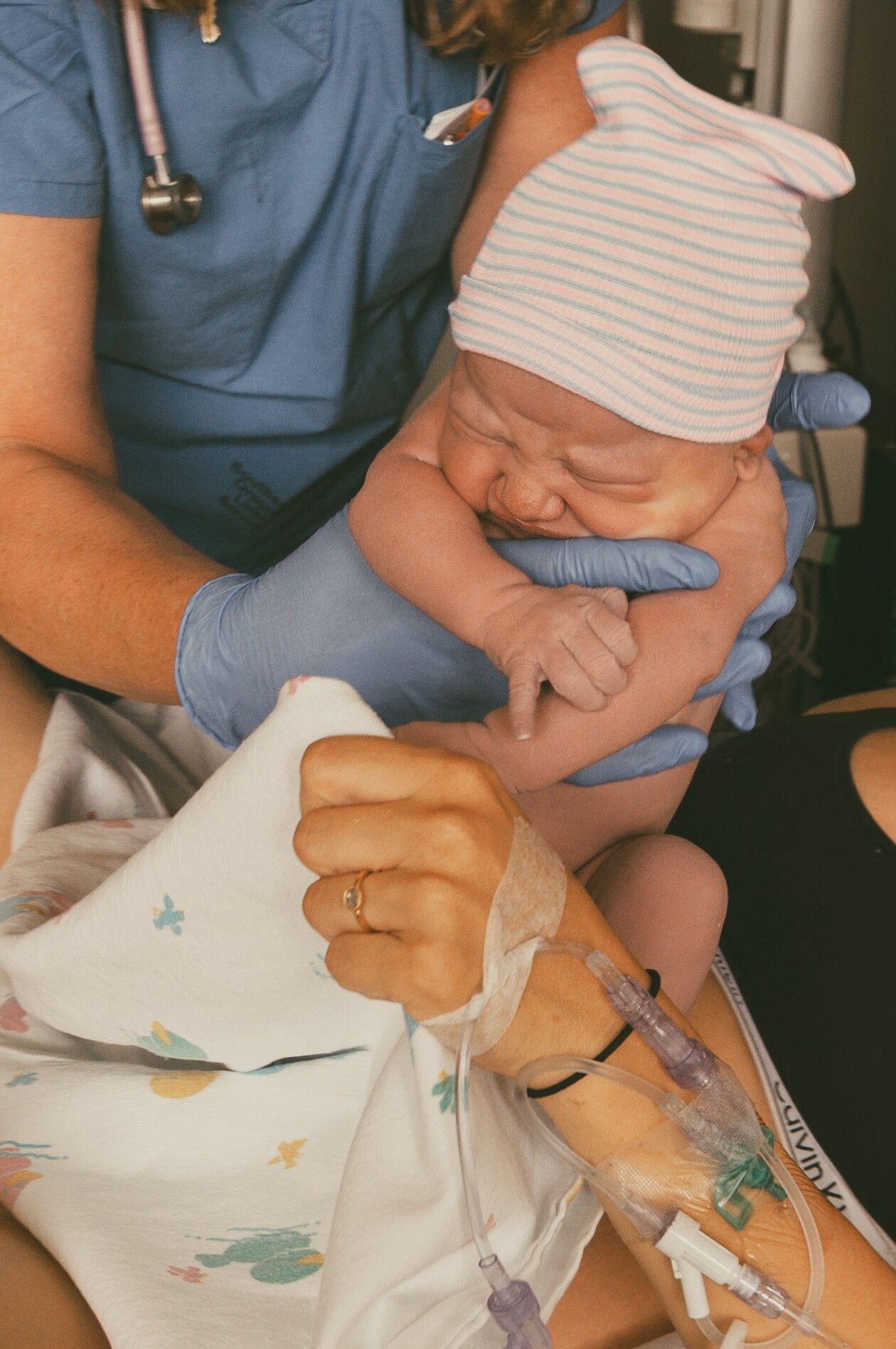 Healthcare worker in blue scrubs holding newborn baby toward new mother.