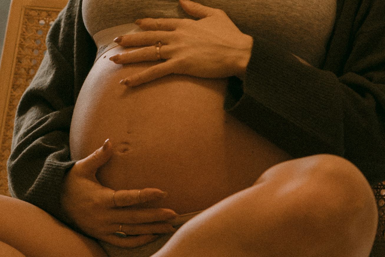 Close-up of pregnant belly gently embraced by two pairs of hands in warm toned maternity photo.