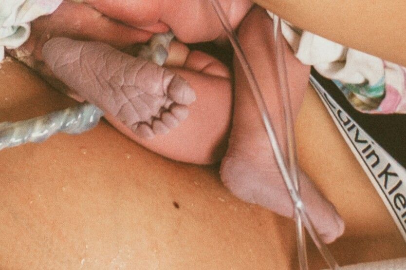 Close-up of newborn baby's tiny feet resting on mother's chest.