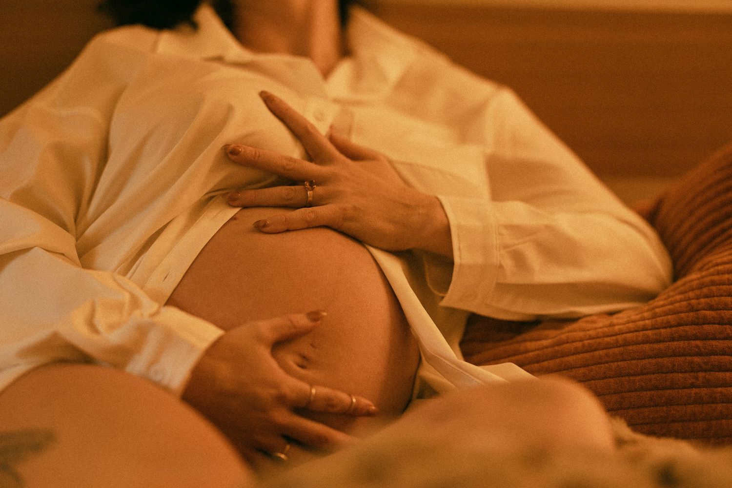 Couple tenderly holding pregnant belly together in cozy warm-toned intimate maternity photography session.