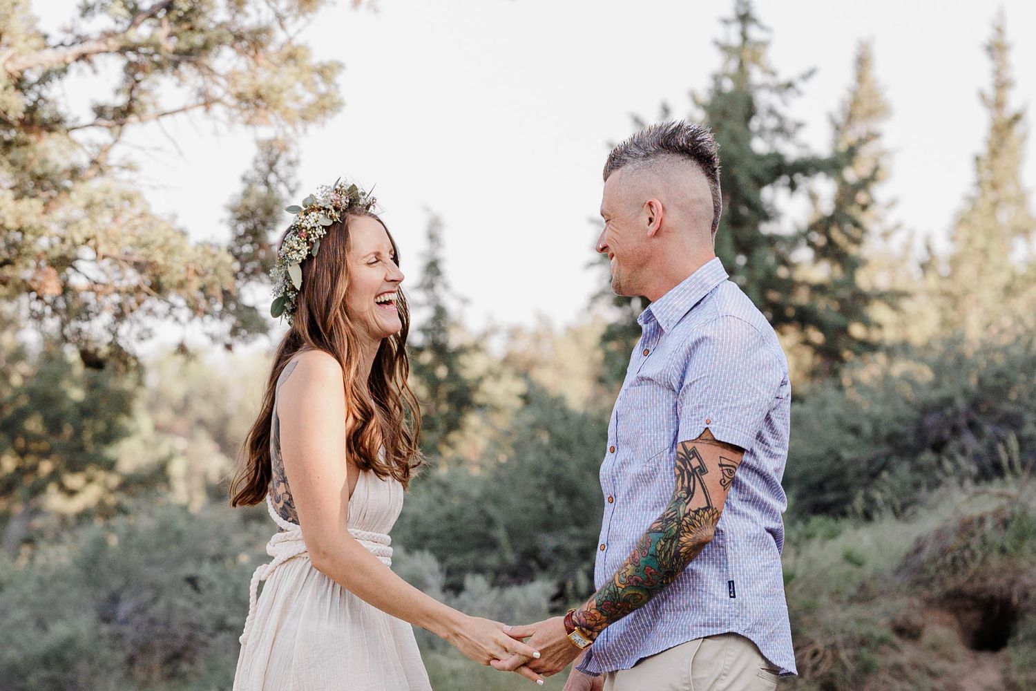Happy couple holding hands and laughing together in a sunny forest setting.