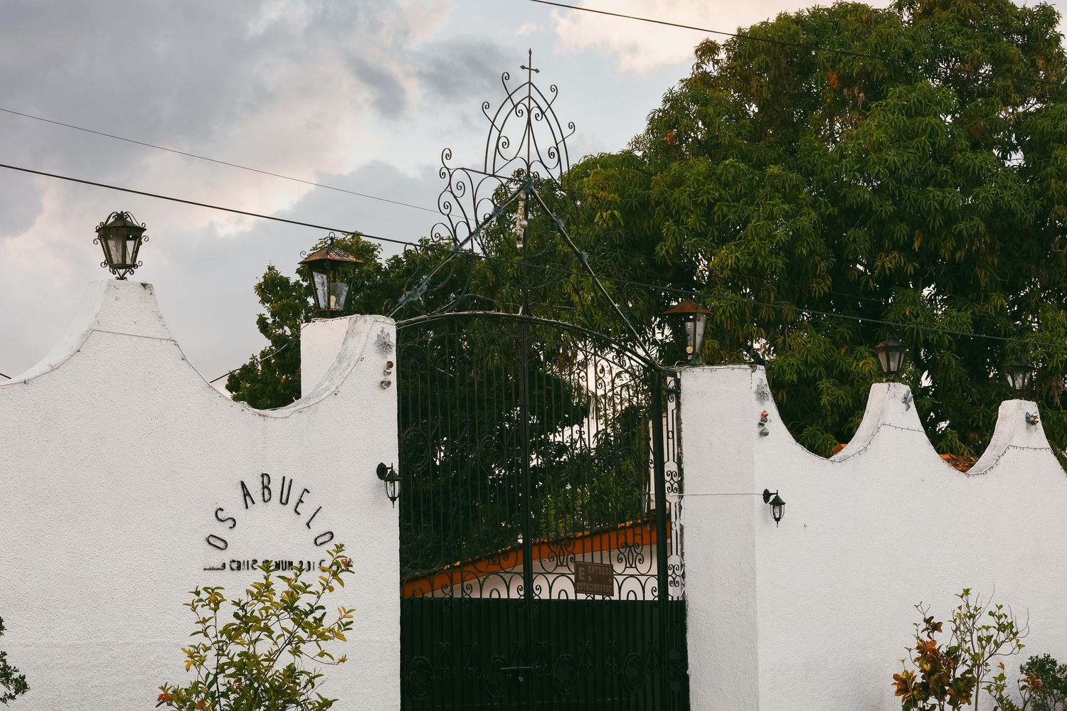 White stucco wall with decorative battlements and ornate black iron gate reading Los Abuelos.