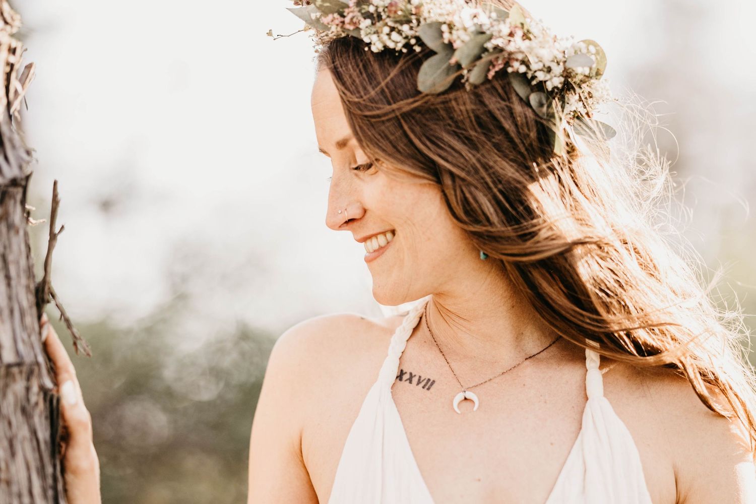 Smiling woman wearing a floral crown and white dress outdoors.