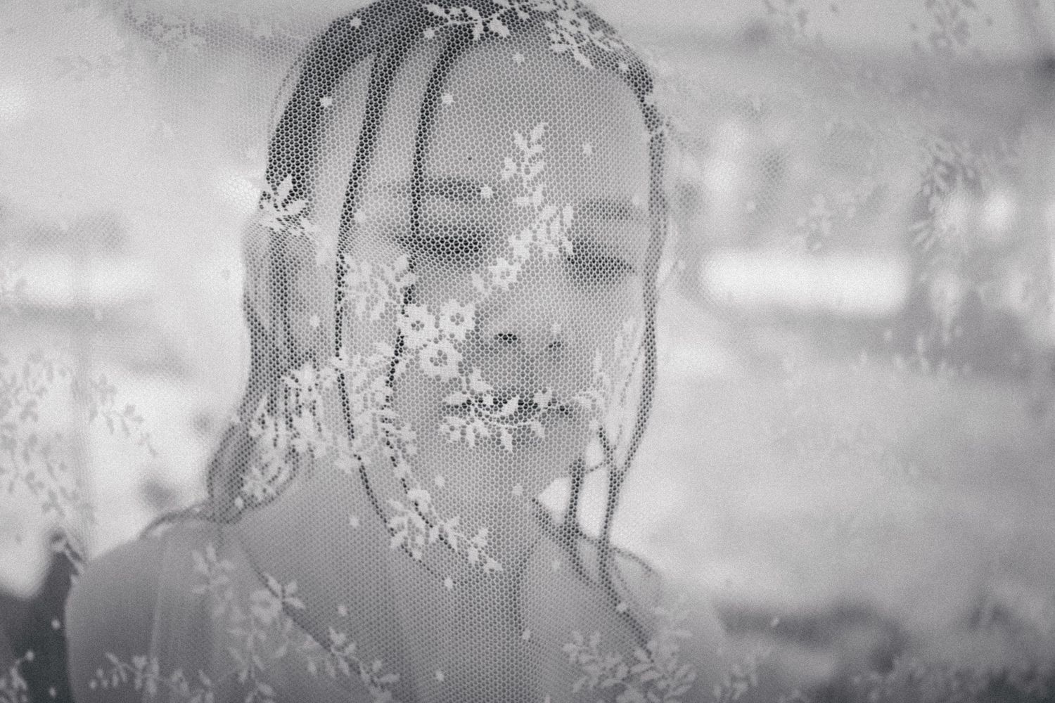 Black and white portrait of a young girl through sheer floral lace fabric.
