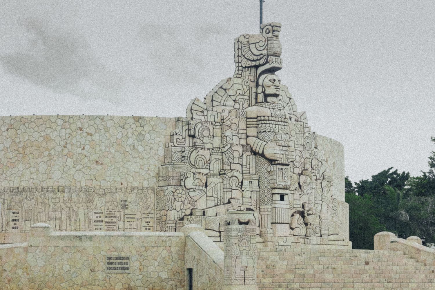 Ancient Mayan stone monument with intricate carvings of a figure against a cloudy sky in Mexico.
