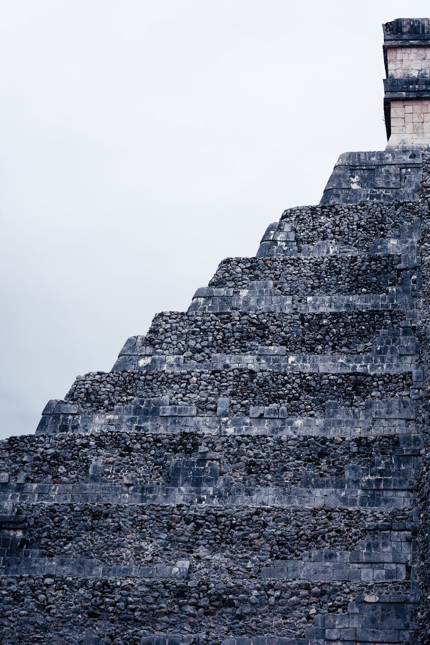 Close-up of ancient Mayan pyramid stone steps at Chichen Itza under overcast sky.
