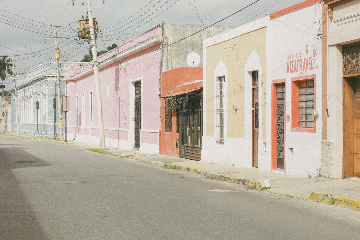 Quiet street lined with pastel-colored colonial buildings under overcast skies in a Mexican town.