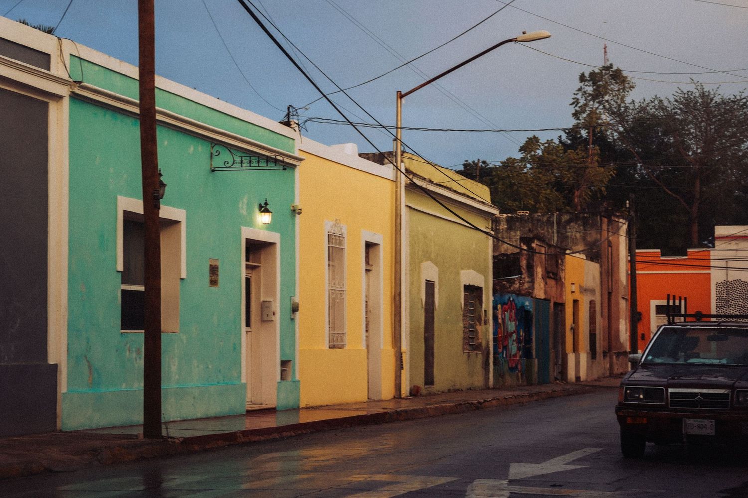 Vibrant colorful colonial buildings in teal, yellow, and orange lining a quiet street at golden hour.