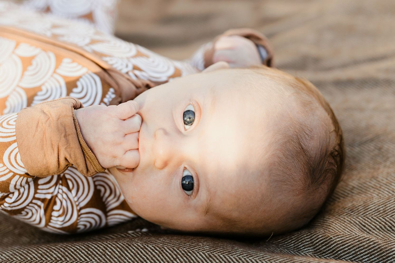 Close-up of a newborn baby in a brown wave-print onesie lying on a blanket.