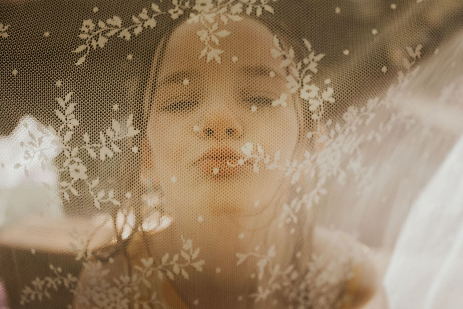 Young woman photographed through a floral lace veil in warm golden tones.