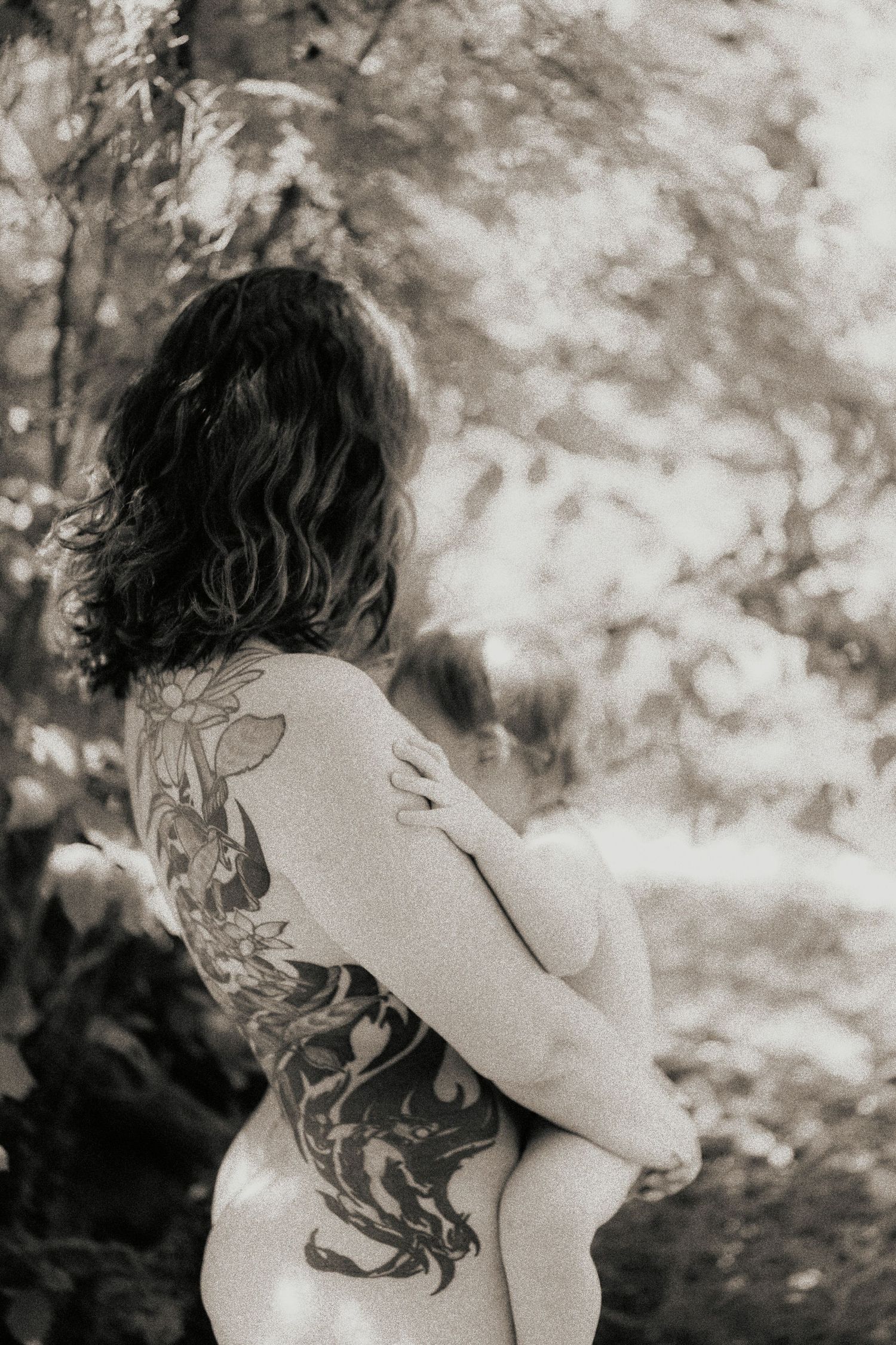 Black and white photo of woman with floral back tattoo in nature.