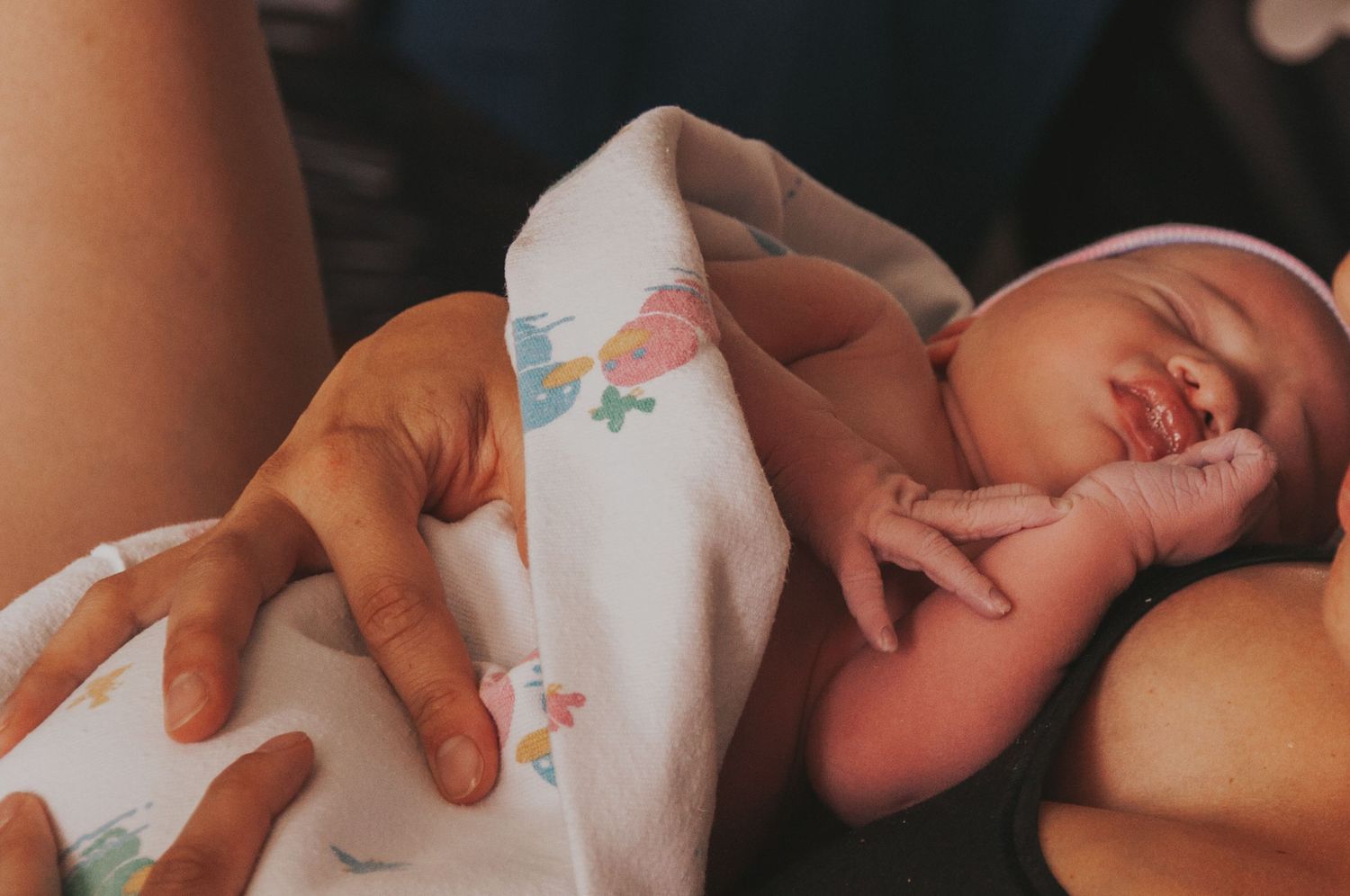 Peaceful sleeping newborn wrapped in floral blanket cradled in arms.