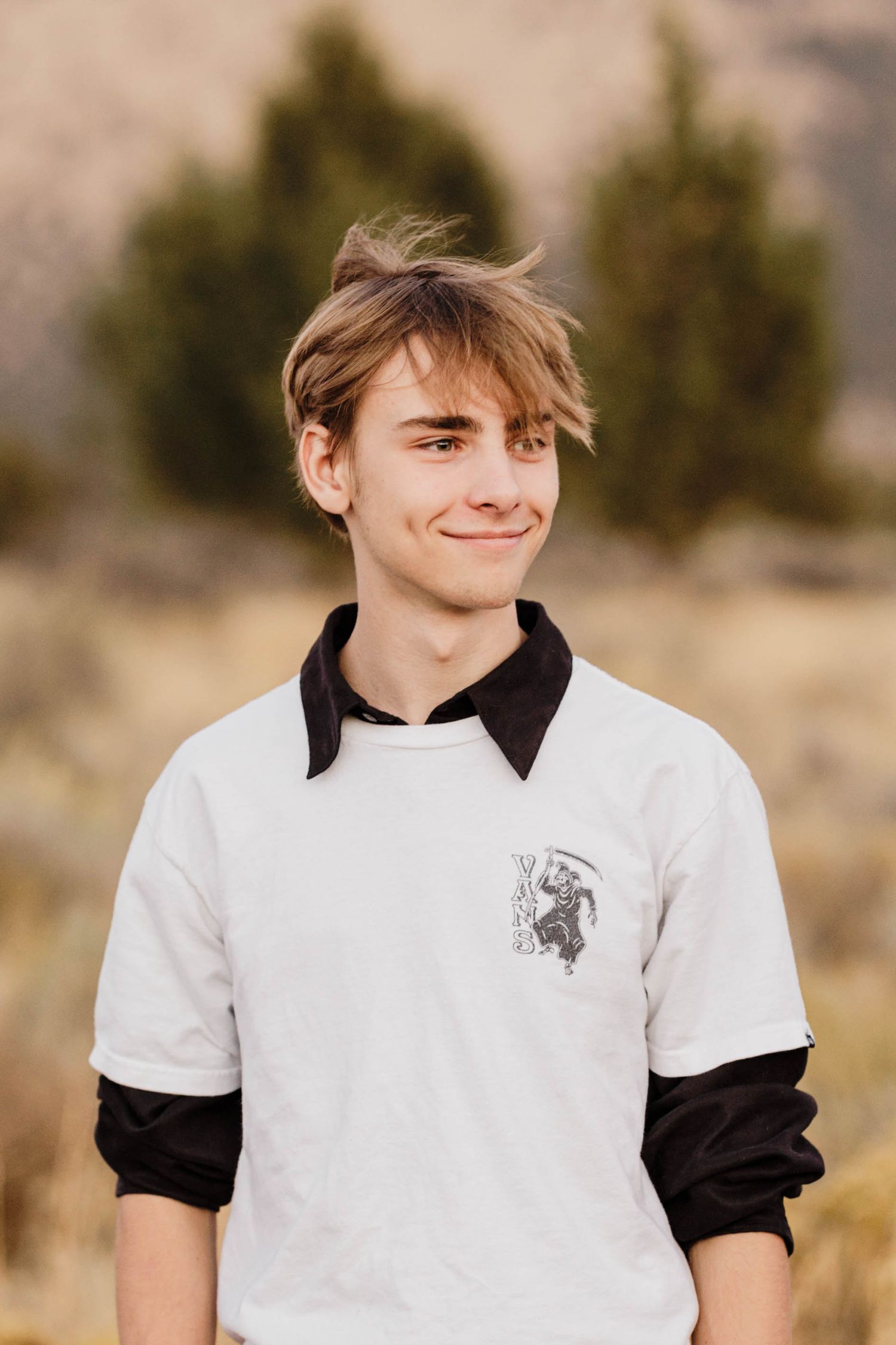 Smiling teenage boy with blonde hair wearing white and black layered shirt outdoors.