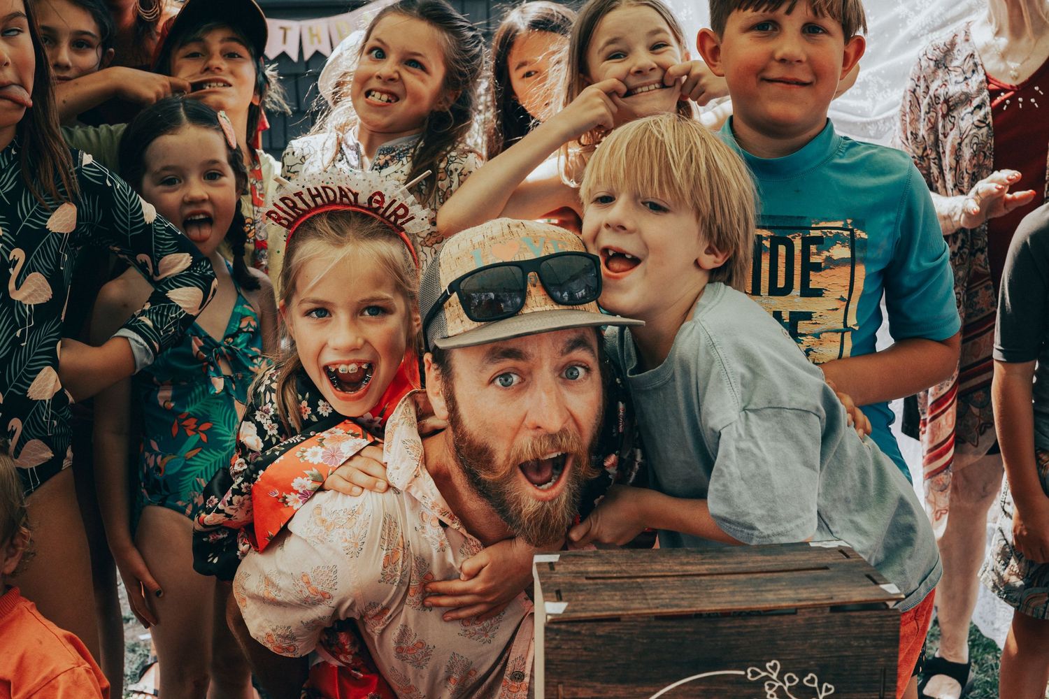 Man in box surrounded by excited children at birthday party celebration.
