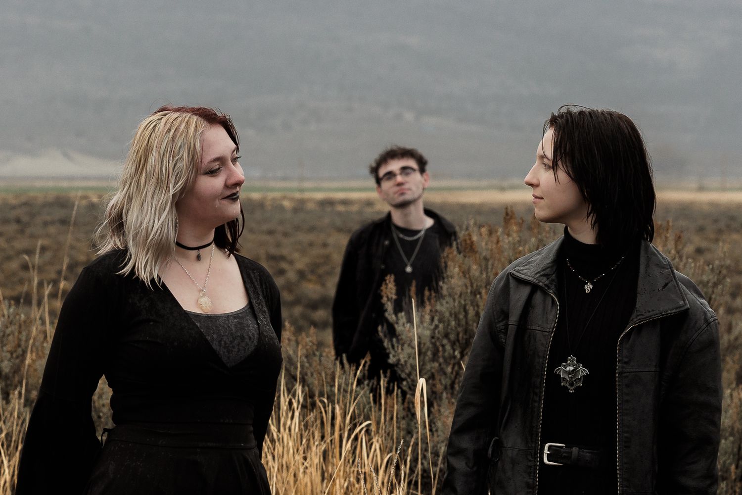 Three people in dark clothing standing in a golden field with misty mountains behind them.