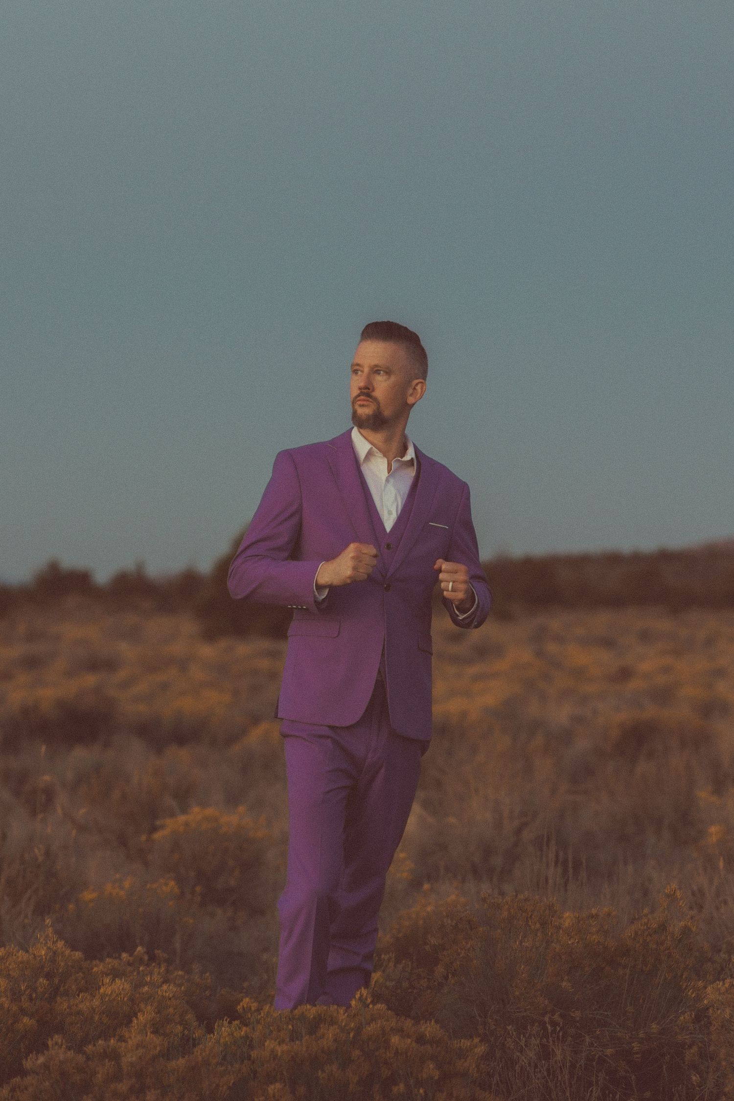 Man in purple suit standing in desert field under clear blue sky at golden hour.