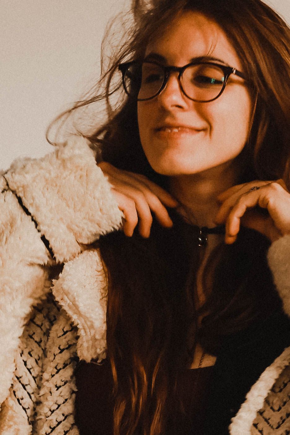 Smiling young woman with glasses and long brown hair wearing a cozy white sherpa jacket.