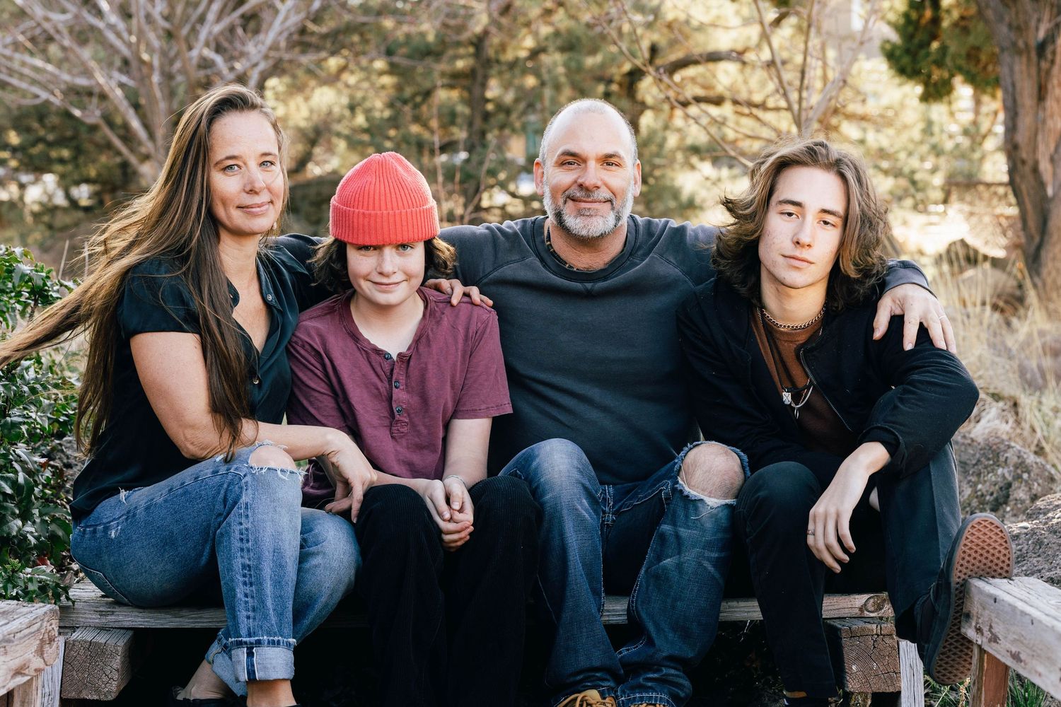 Family of four smiling together seated outdoors in a garden setting.