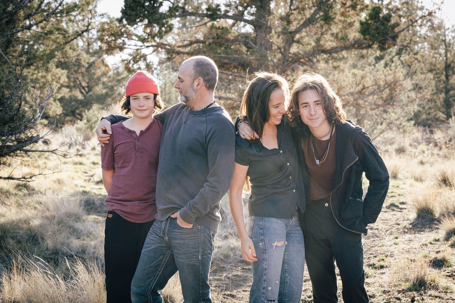 Family of four standing close together smiling in a natural outdoor setting.