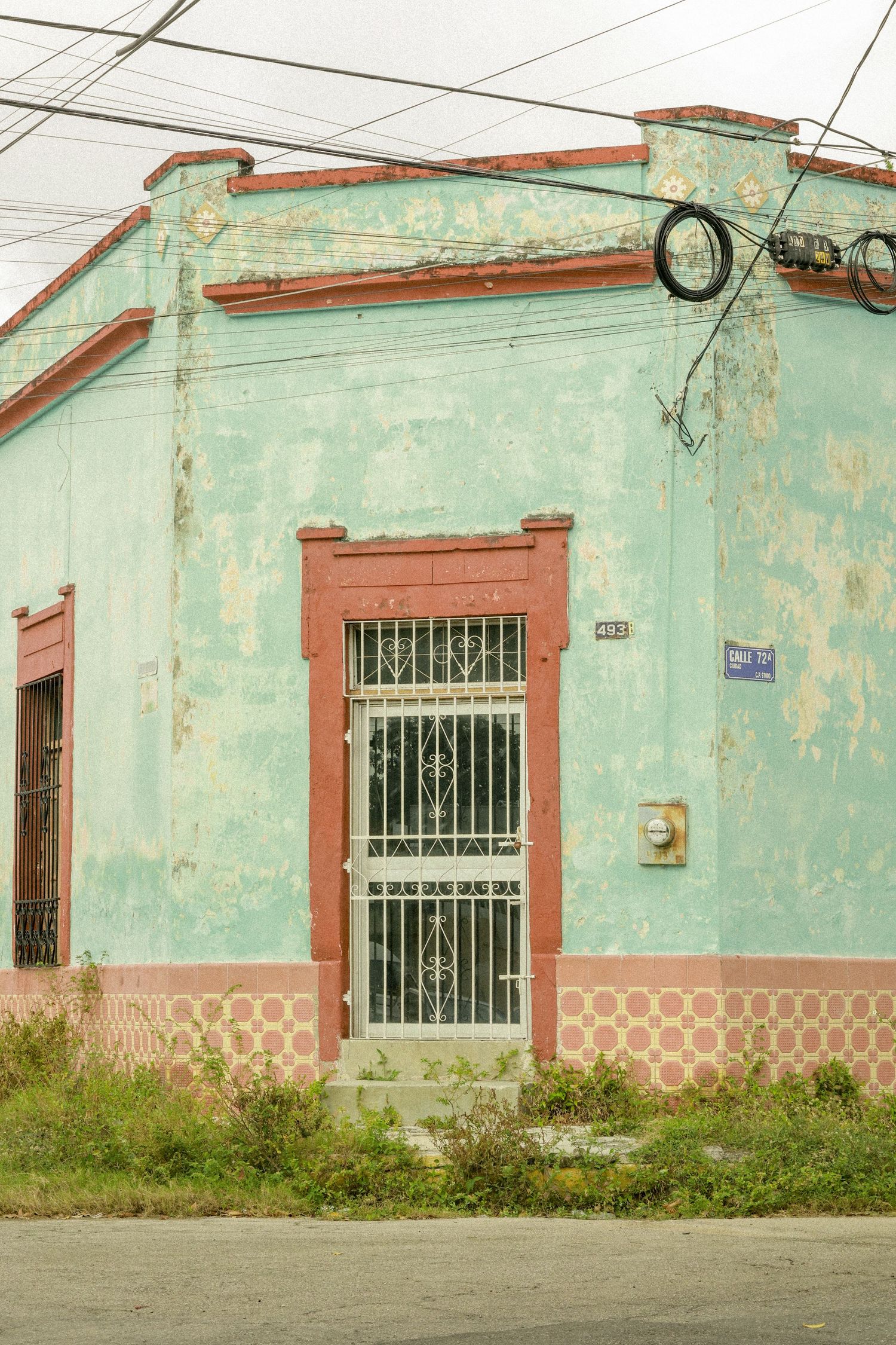 Weathered mint green and terracotta colonial corner building with barred door and peeling paint.