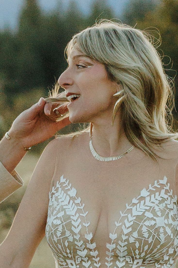 Smiling blonde bride in lace wedding dress sipping champagne outdoors at golden hour.