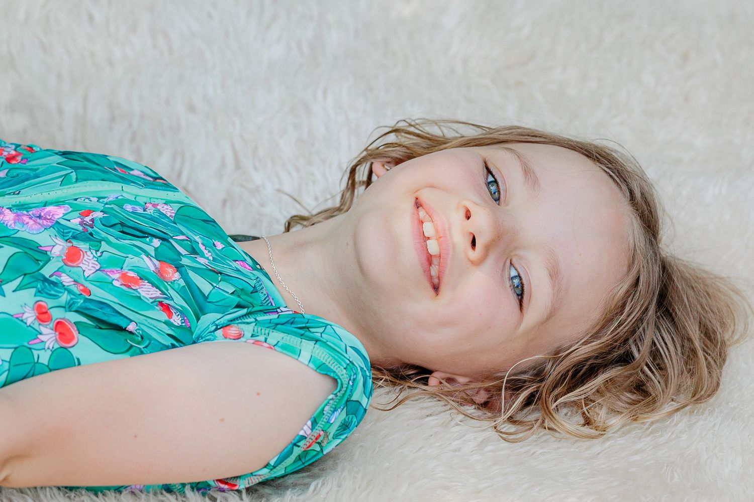 Happy young girl with blue eyes smiling while lying on a white fluffy rug.