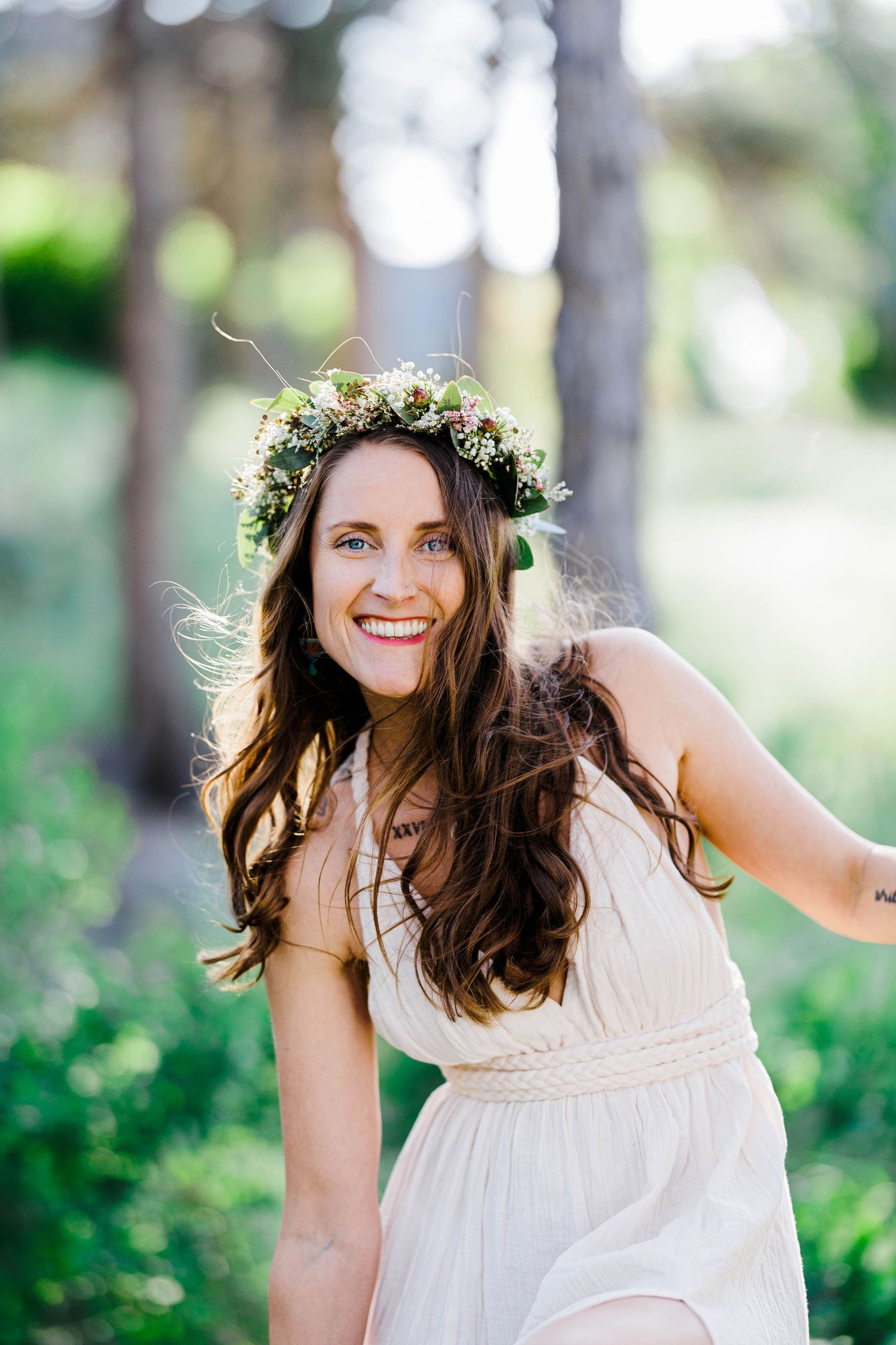 Happy woman in floral crown and white dress smiling in a forest.