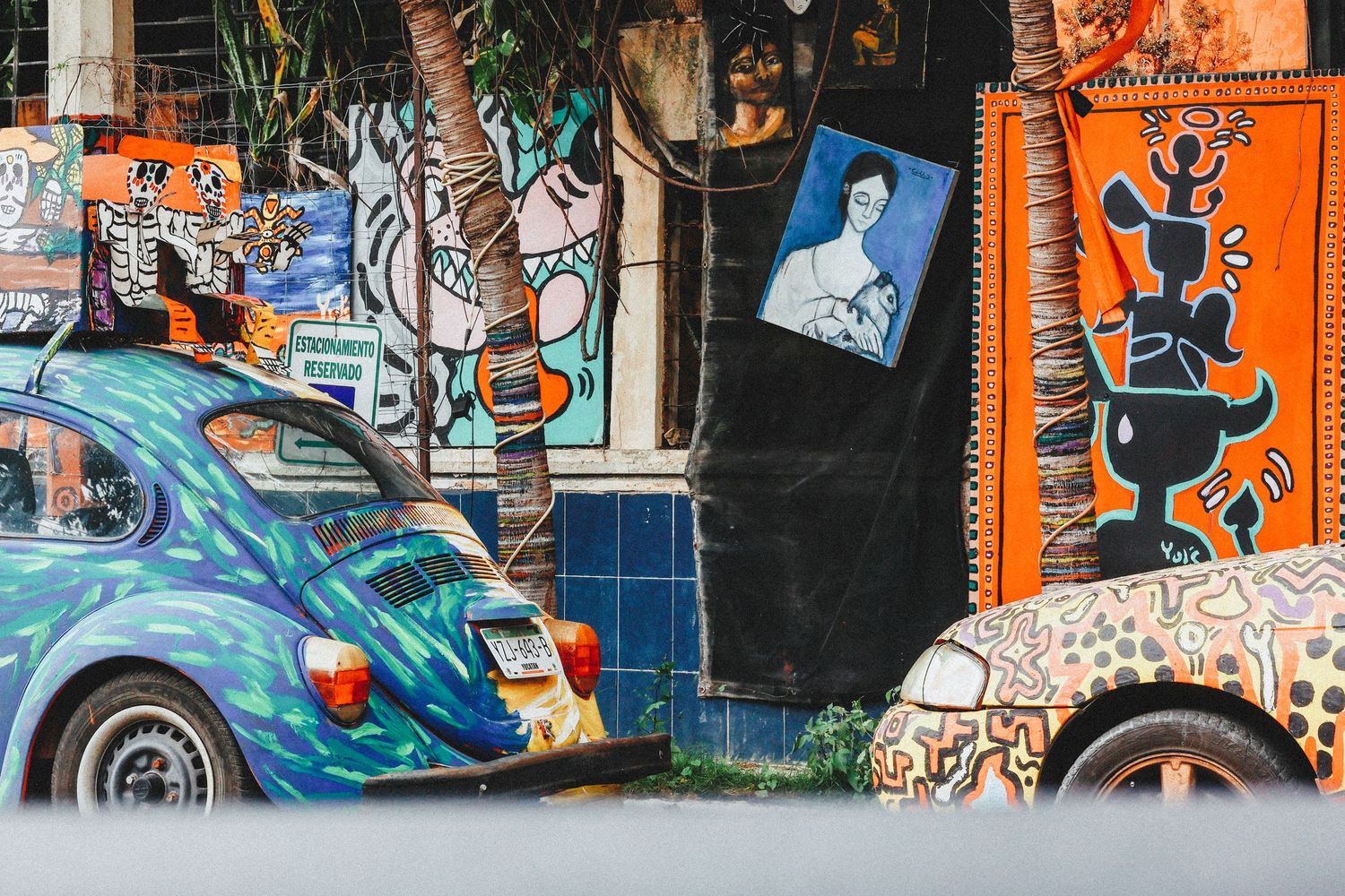 Colorful street art murals with painted Volkswagen Beetle cars parked outside a vibrant urban art gallery.