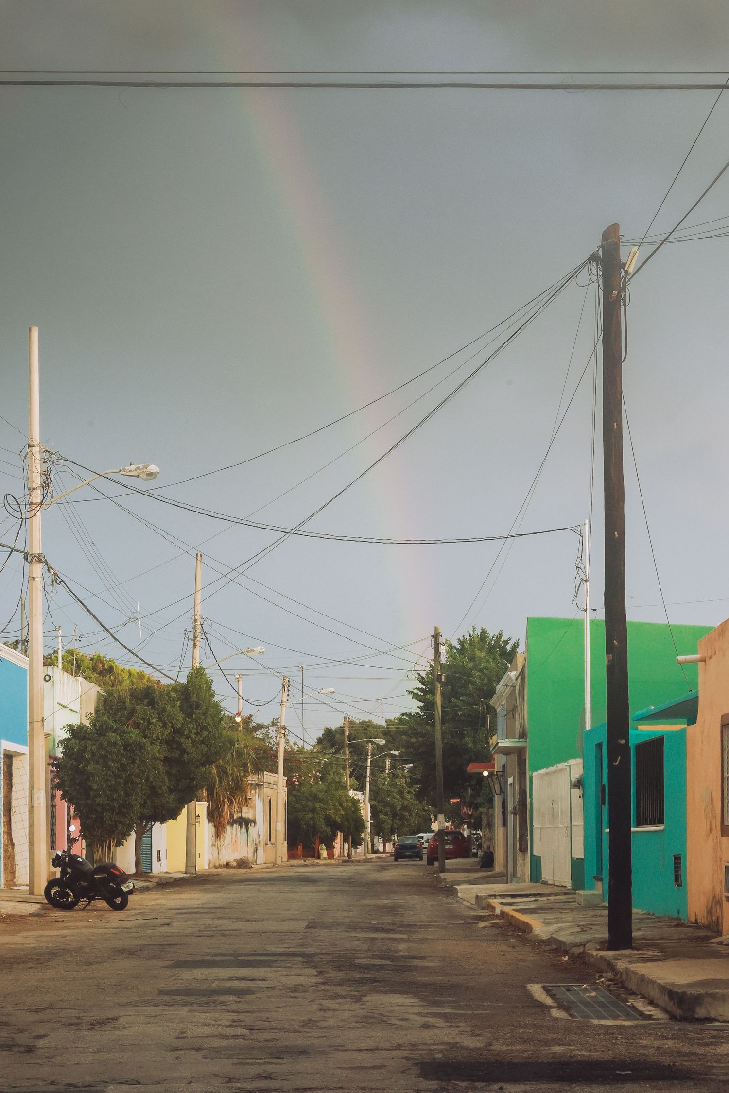 Quiet street lined with colorful buildings and utility poles with a rainbow arching across the sky.