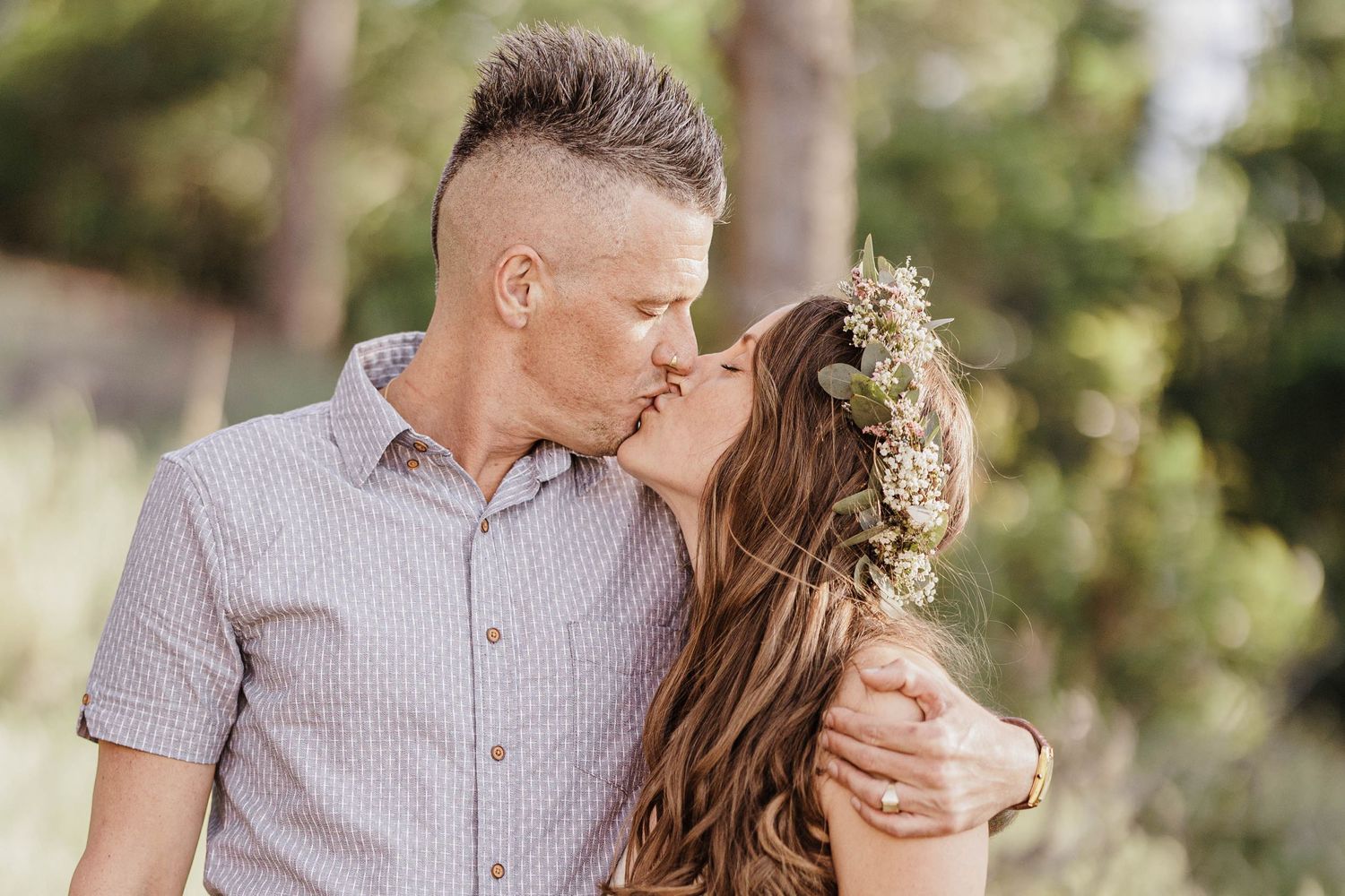 Couple sharing a kiss outdoors, woman wearing a green floral crown.