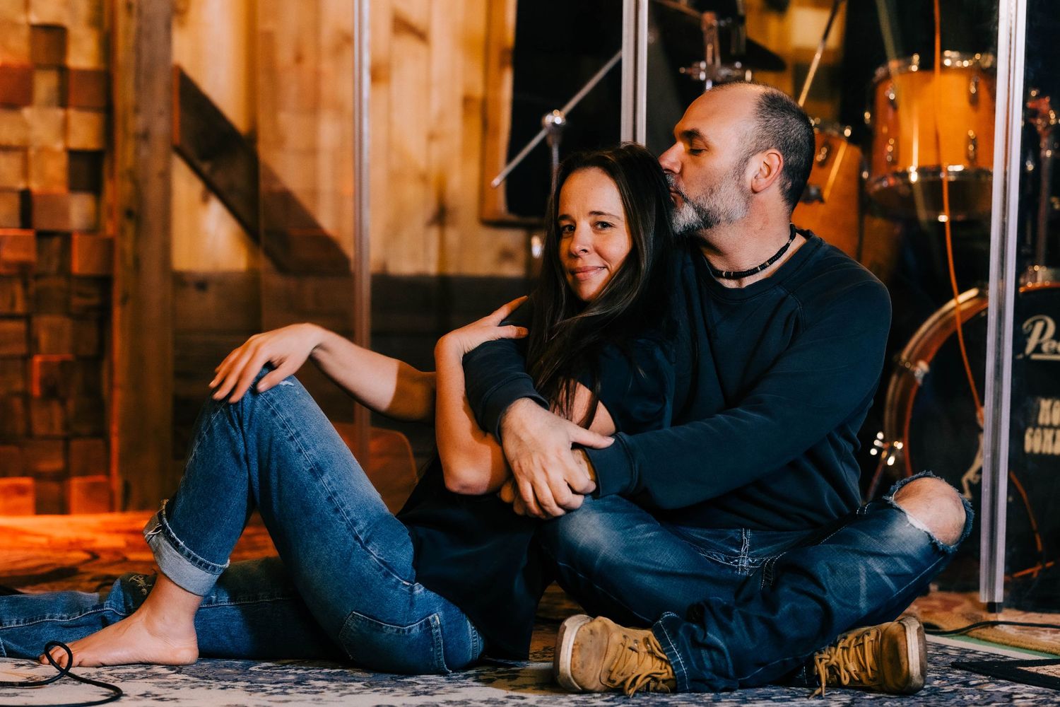 Smiling couple sitting closely together on the floor inside a warmly lit music studio.