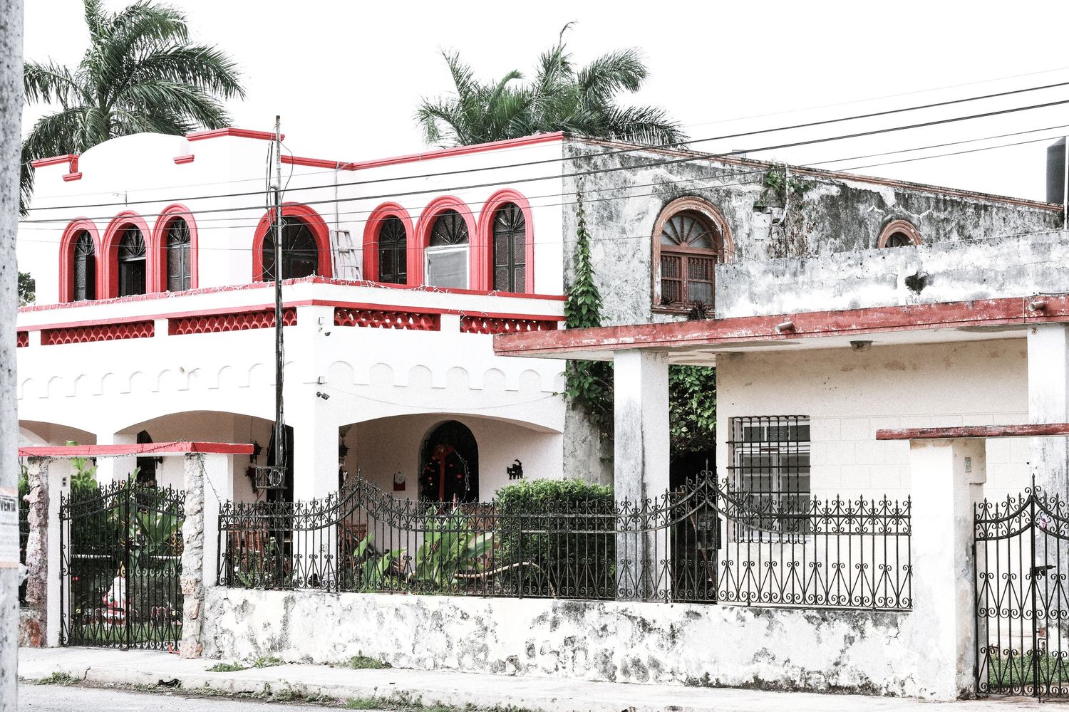 White and red colonial-style house with ornate ironwork fence and palm trees in Mexico.