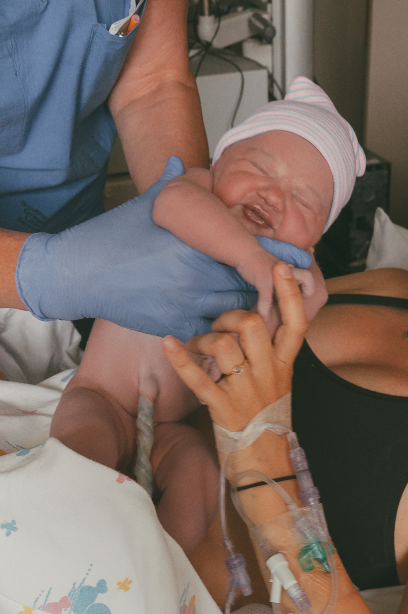 Medical professional presenting crying newborn to mother in delivery room.