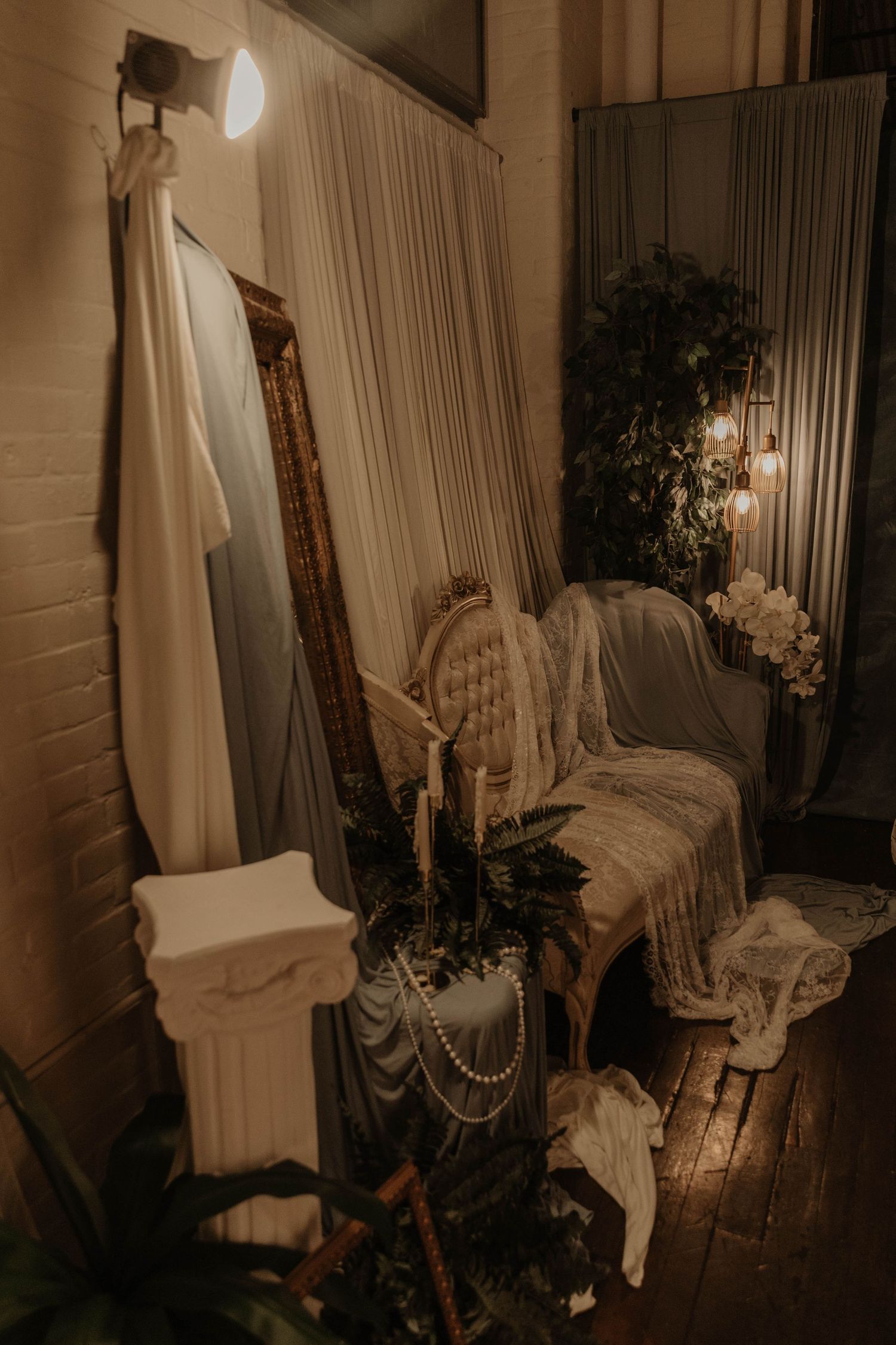 Elegant vintage wedding decor with ornate mirror, tufted chair, pearls, candles, and white draping.