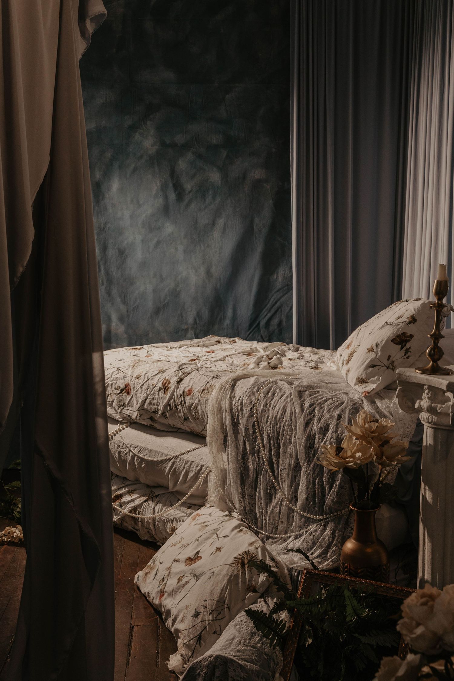 Romantic bohemian bedroom with floral bedding, fringe blanket, candle holder, and moody dark walls with draped curtains.