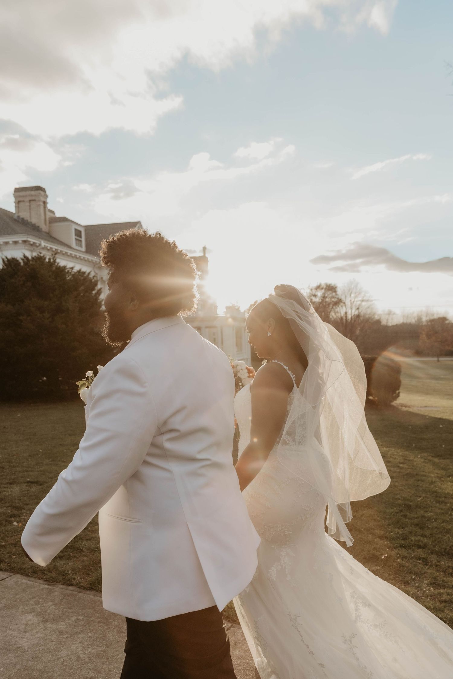 Bride and groom walking in golden sunset light outside an elegant white colonial wedding venue.