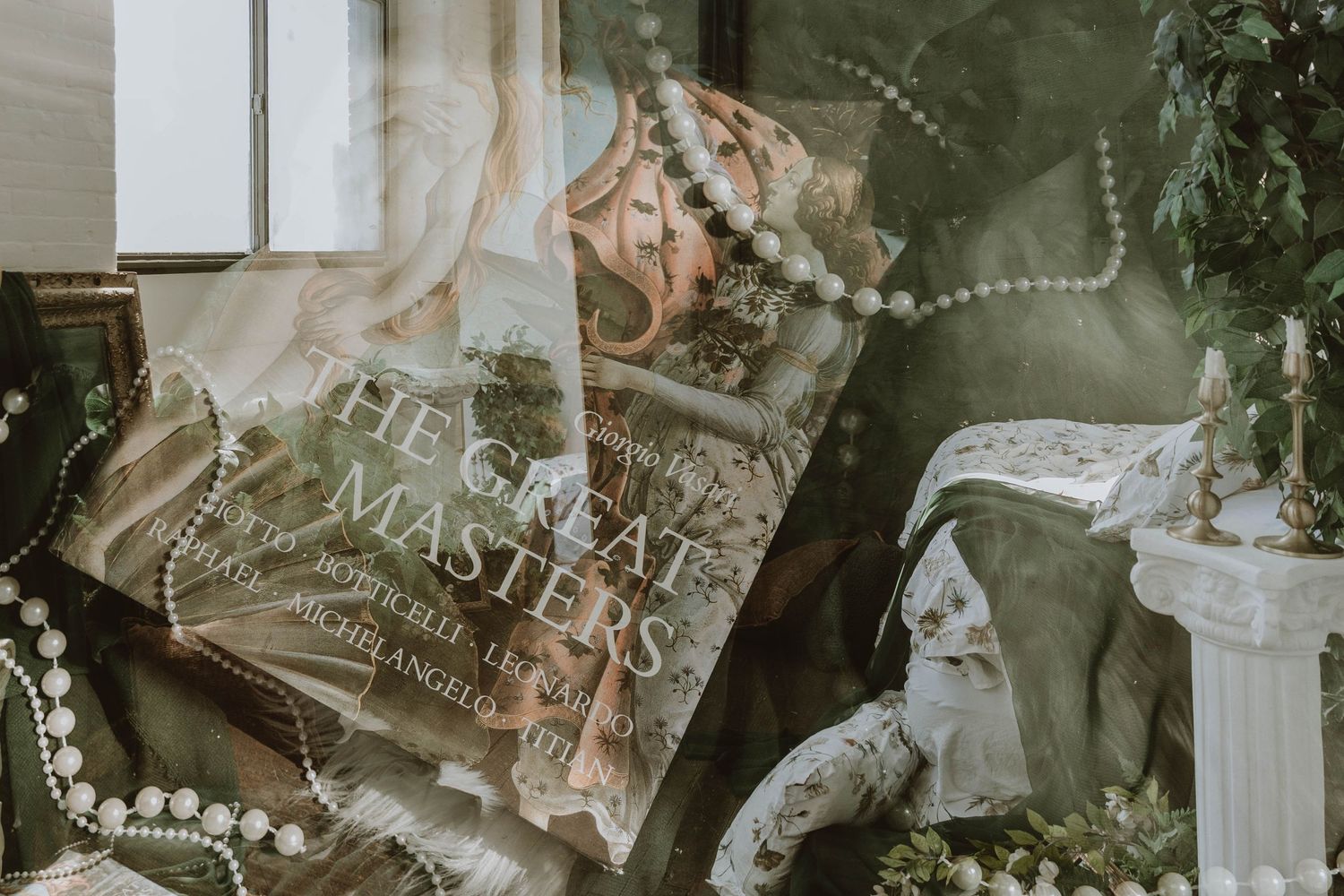 Vintage book 'The Great Masters' surrounded by pearl necklaces, lace, and greenery in an elegant styled flat lay.