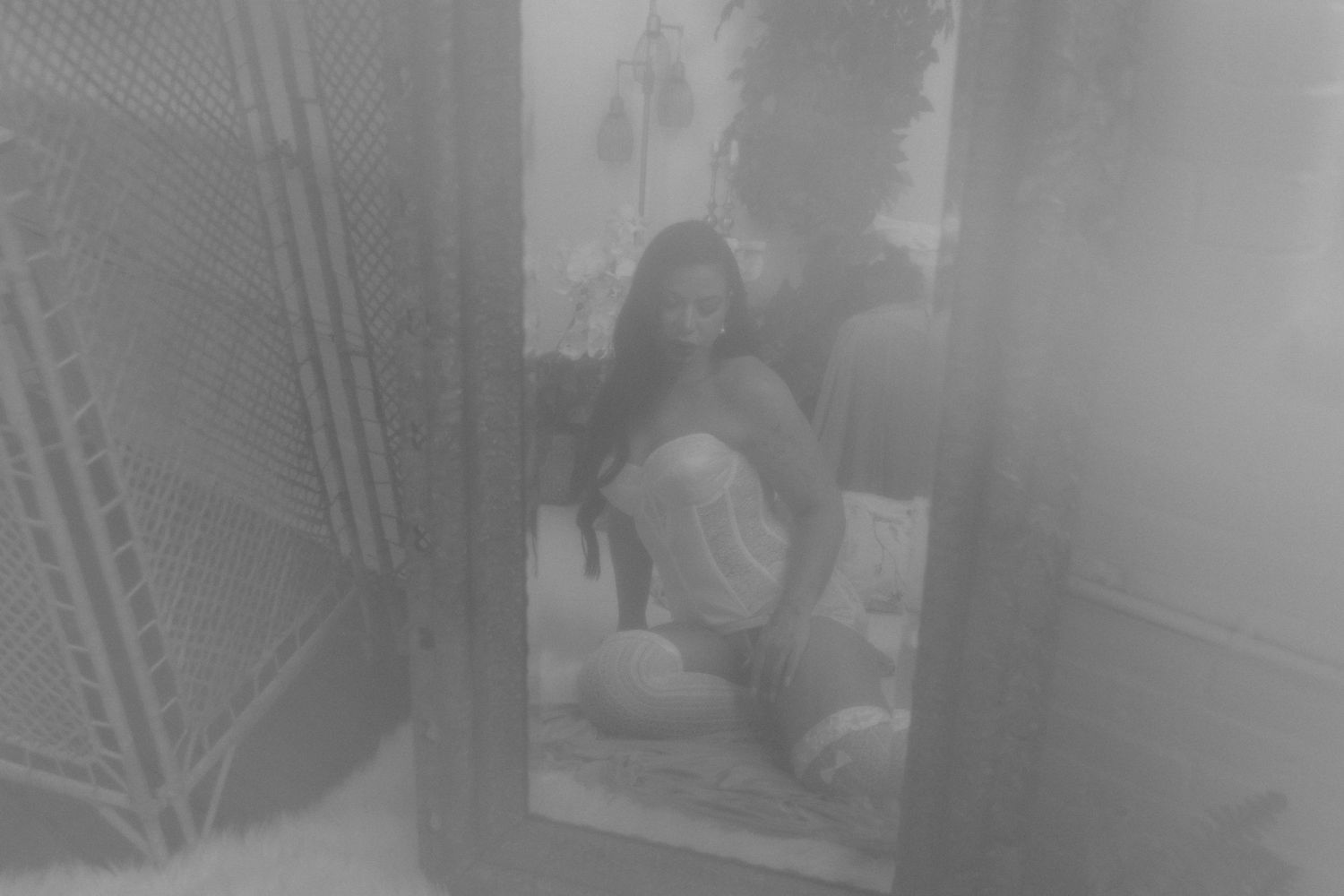 Black and white photo of a woman with long hair sitting and reflected in a mirror indoors.