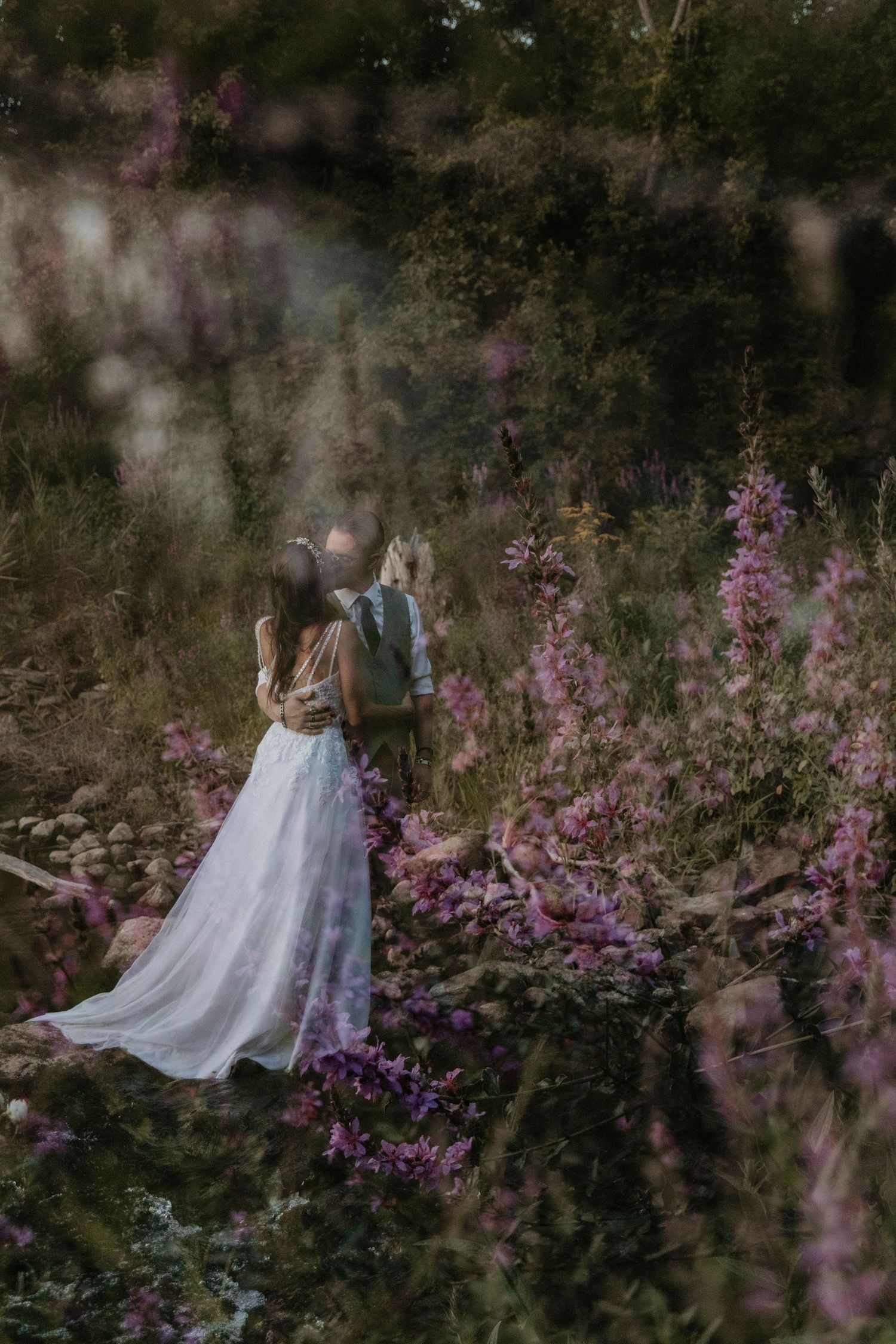 Bride and groom embracing among wild purple flowers in a lush garden setting during outdoor wedding.