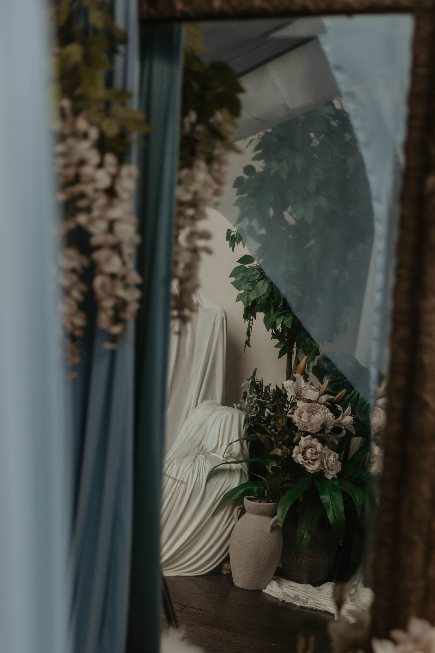 Mirror reflection of elegant floral arrangement with peonies, greenery, and draped white fabric in a styled interior.