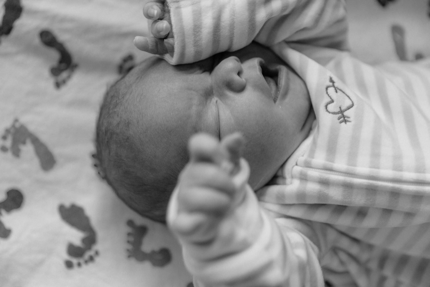 Black and white close-up of peaceful newborn baby in striped outfit on footprint blanket. top rated RI birth photographer