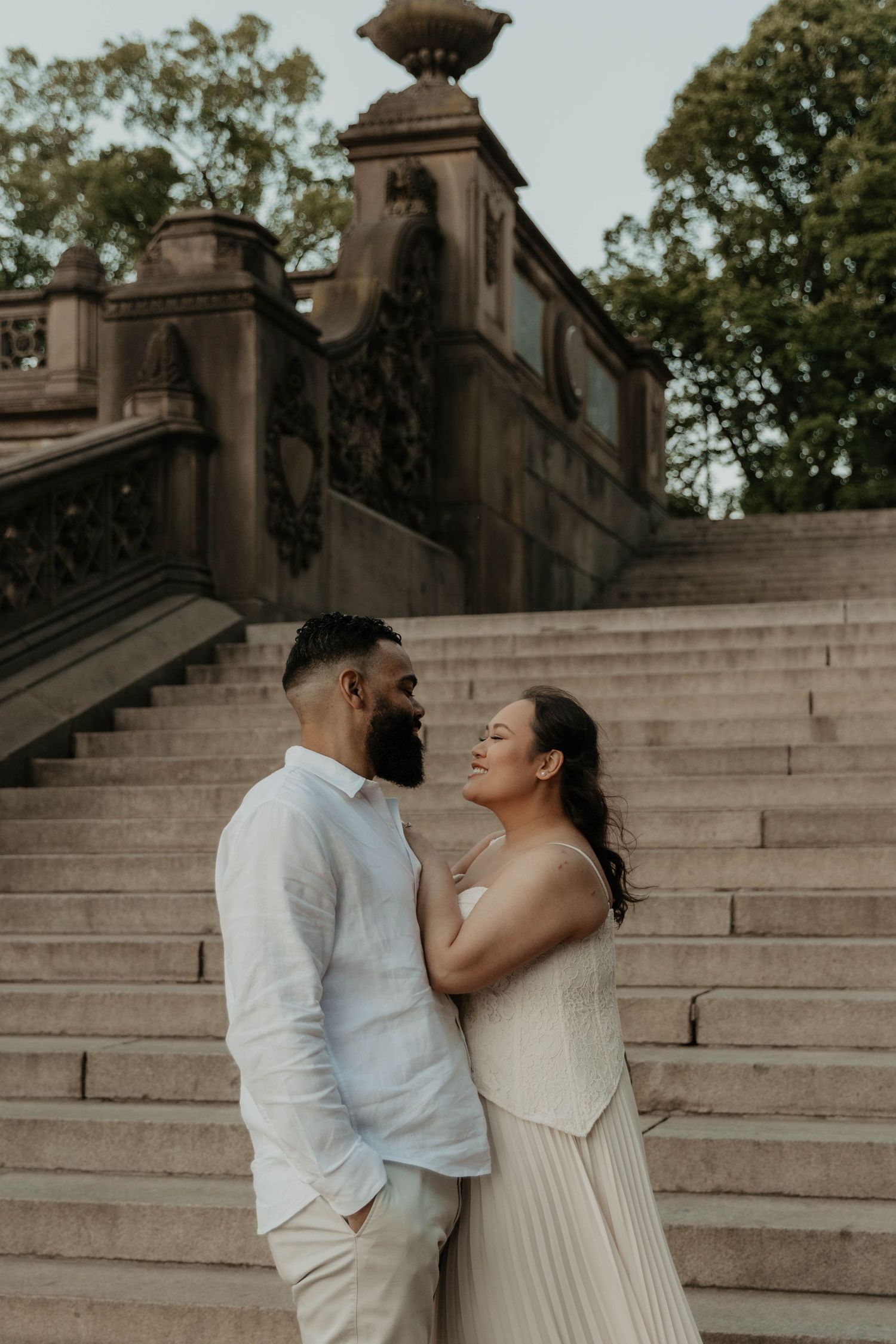 A couple in white attire shares a romantic moment on stone steps at Bethesda Terrace in Central Park, NYC.