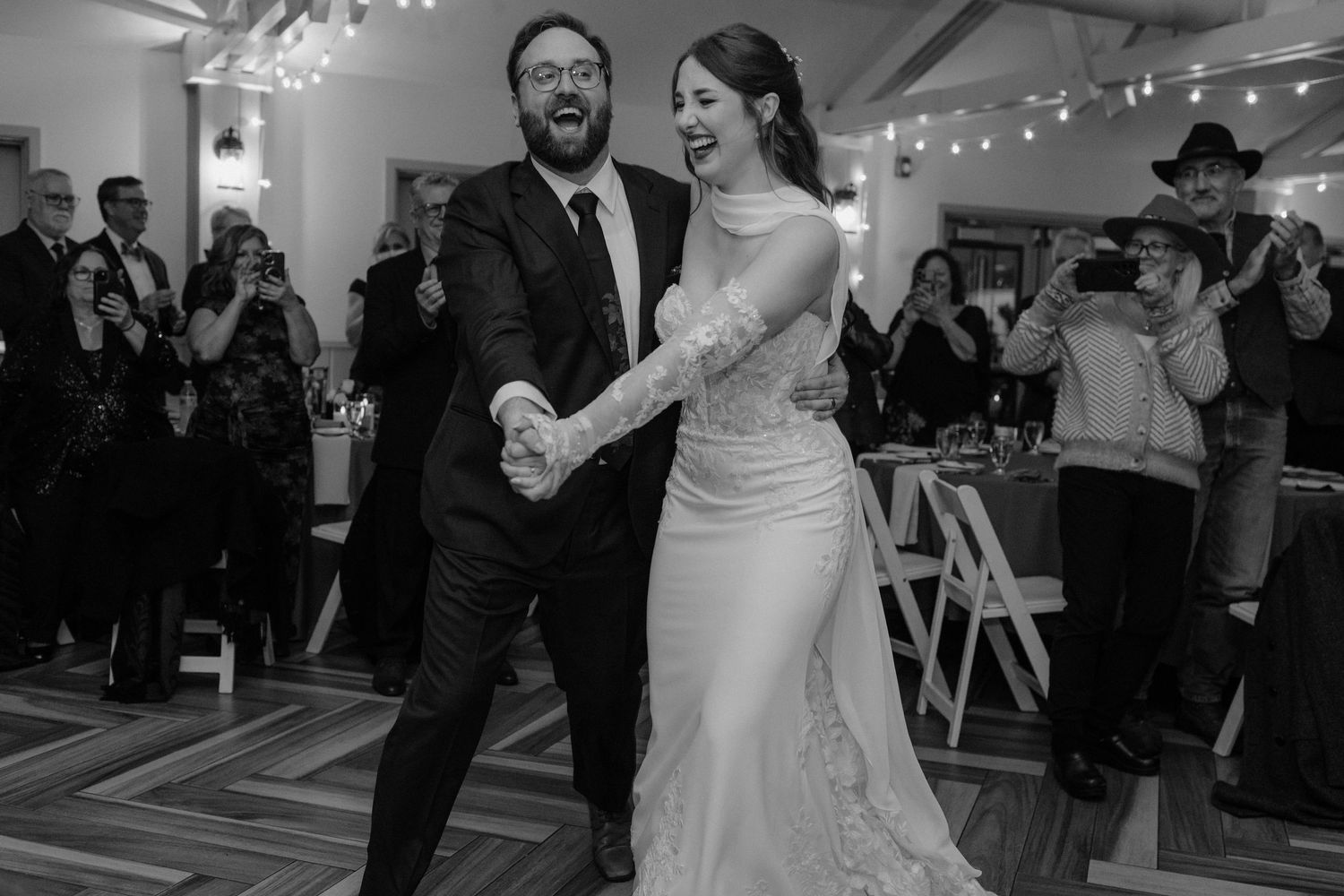 Black and white photo of laughing bride and groom holding hands during first dance at wedding reception. top rated RI wedding photographer