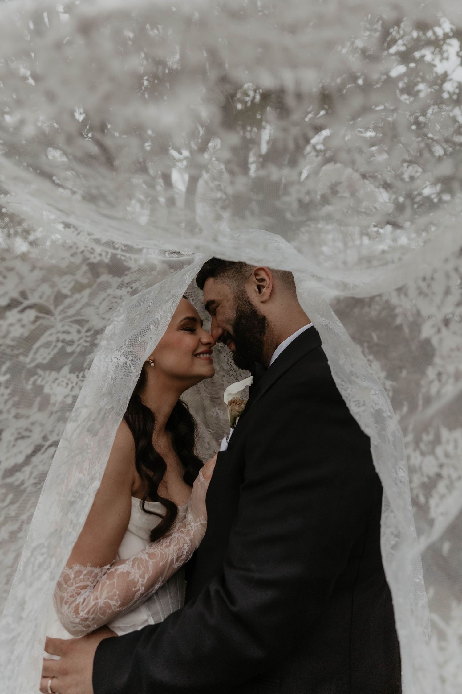 Bride and groom share intimate moment under flowing lace wedding veil in romantic outdoor portrait.

top rated RI wedding photographer