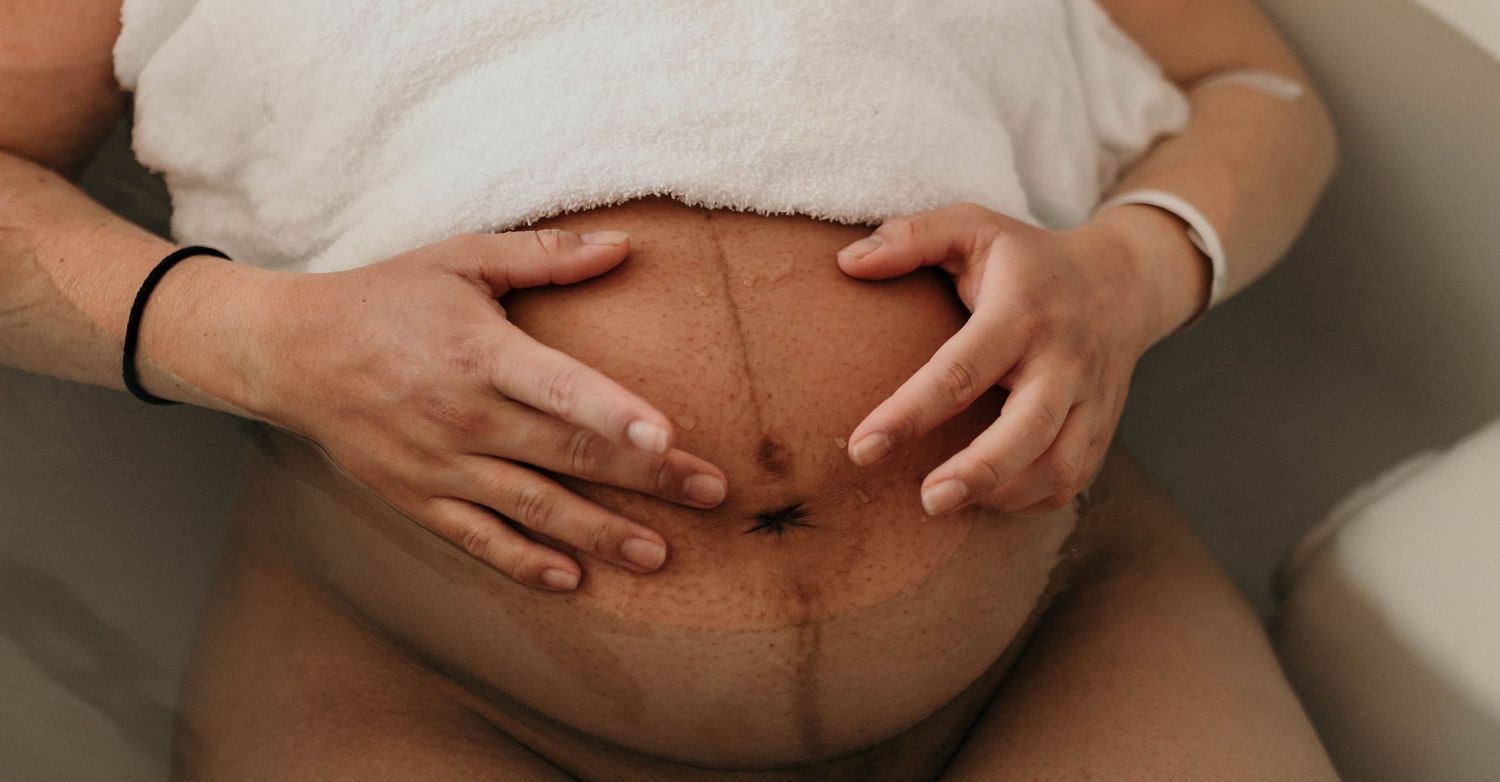 Close-up of pregnant belly with linea nigra, hands gently cradling bump during water birth. top rated RI birth photographer