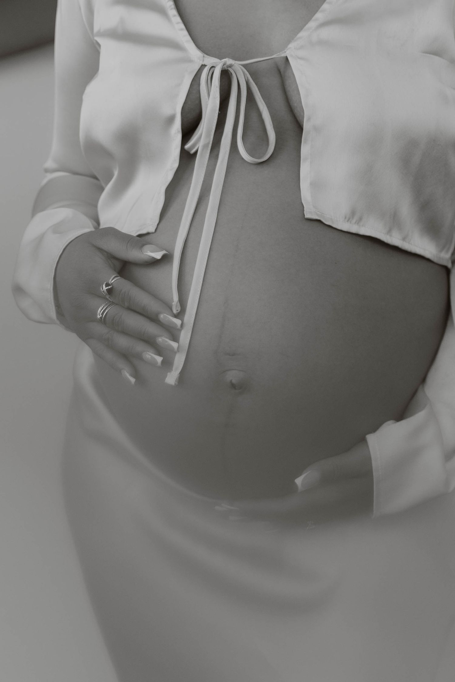 Black and white maternity photo of pregnant woman in white crop top cradling her bare bump. top rated RI maternity photographer