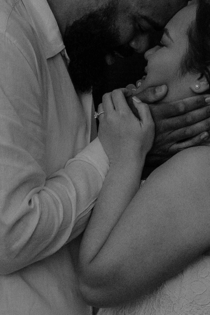 Black and white photo of a romantic couple sharing an intimate moment, woman wearing engagement ring.