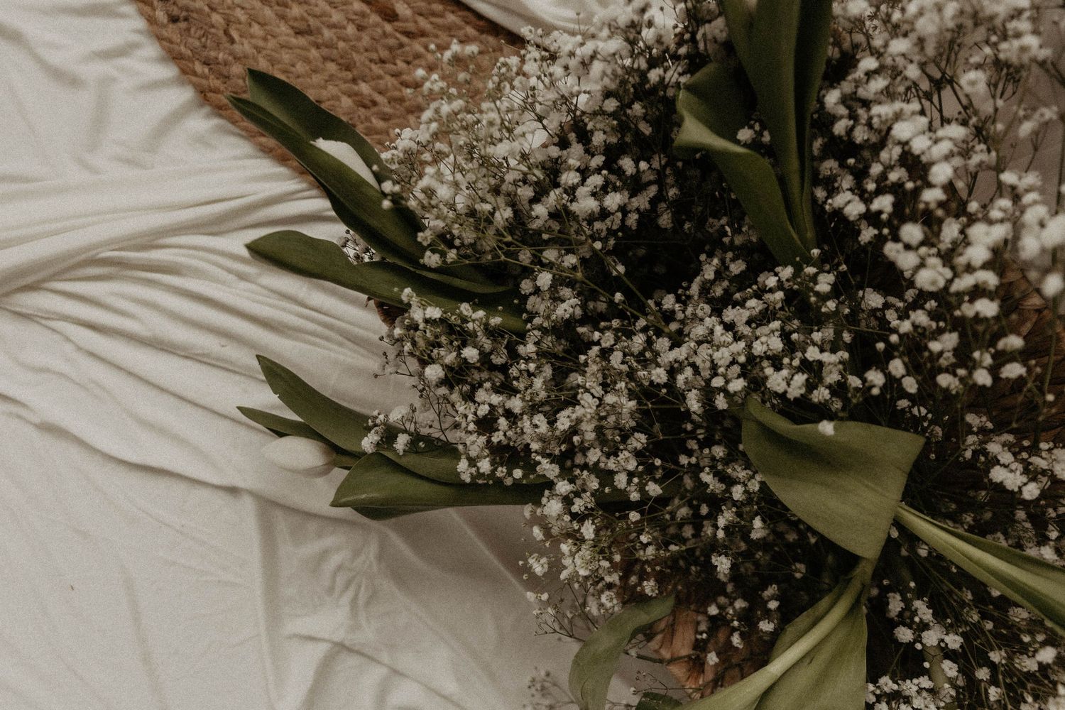 Elegant bouquet of white baby's breath and green tulips arranged on a white linen cloth with a wicker basket.